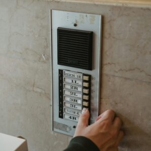 Close-up of a hand pressing an intercom button outdoors on a building wall.